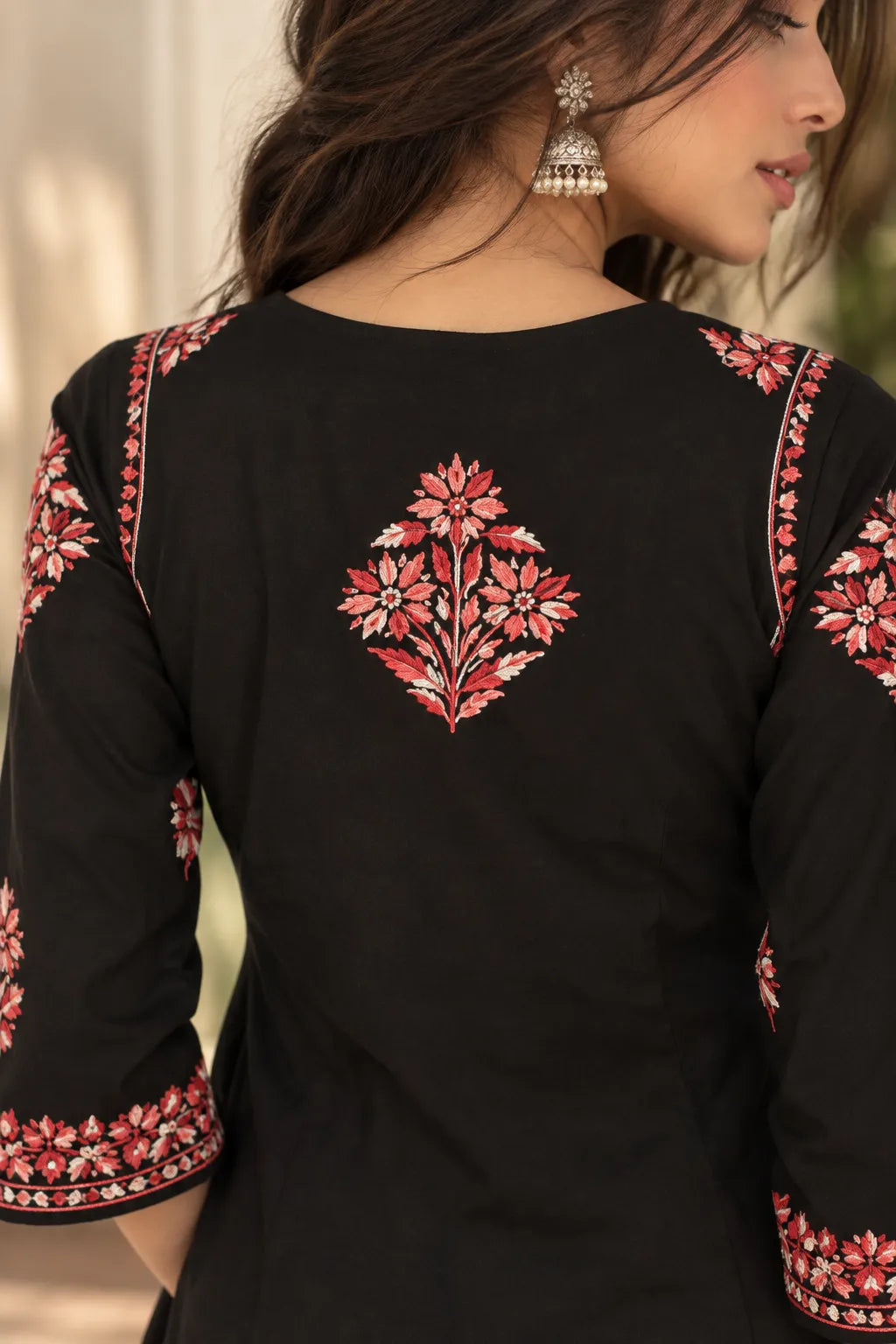 A close-up back view of a woman wearing a black kurta with red and pink floral embroidery on the back and along the sleeve cuffs.