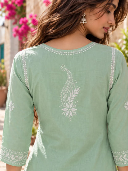 A woman wearing a sage green cotton kurta with white embroidered details on the back, shown in a close-up outdoor shot.