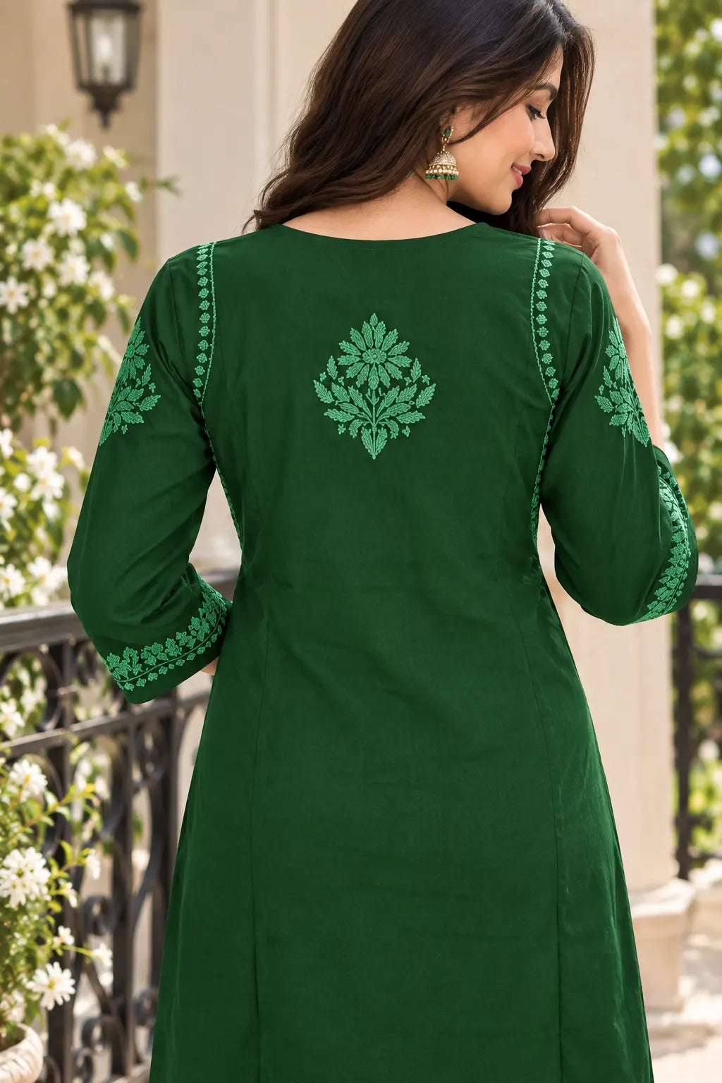 A woman wearing a dark green kurta with light green floral embroidery on the back and sleeve cuffs, photographed outdoors against a light-colored building and greenery.
