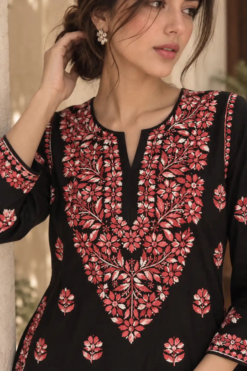 A woman wearing a black kurta with intricate red and pink floral embroidery, featuring a split neckline and 3/4 sleeves.
