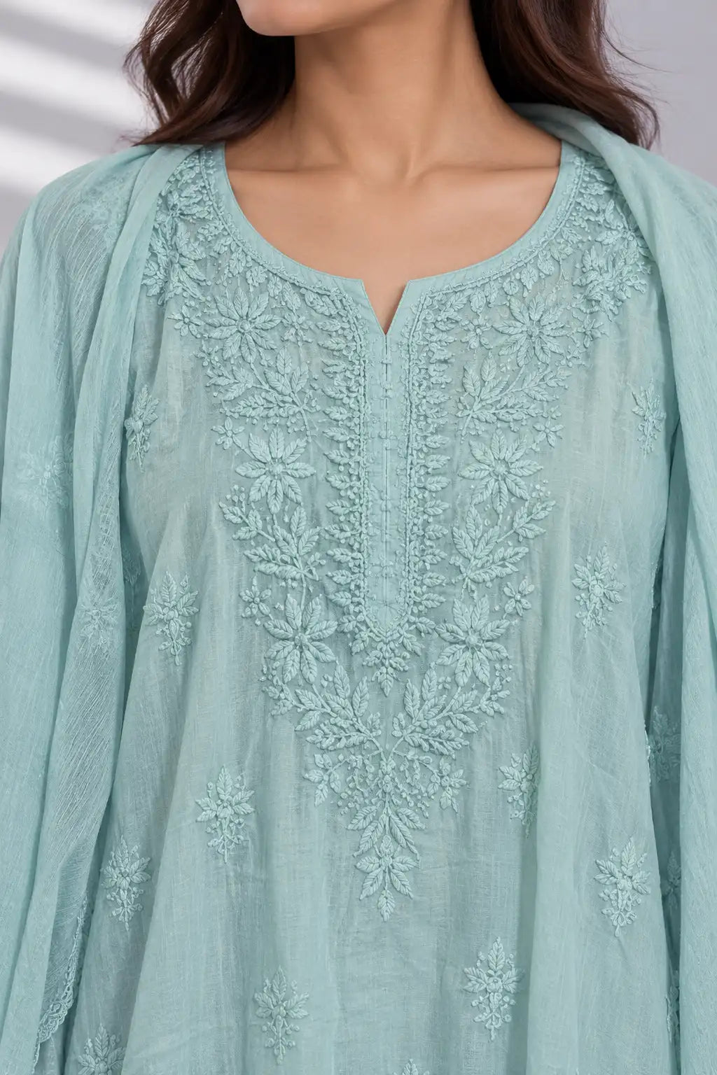 A close-up of a woman wearing a light mint green embroidered kurta with a matching dupatta. The kurta features intricate floral embroidery around the neckline and down the center front, with a split neckline.