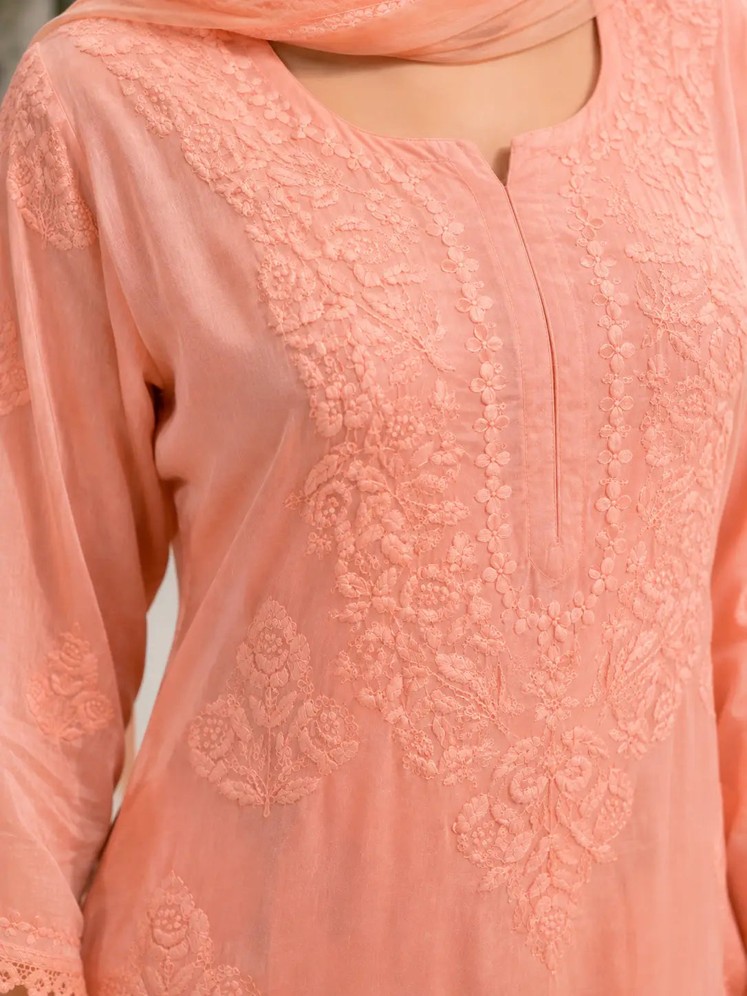 A close-up of a peach-colored embroidered tunic with floral lace detailing and a matching dupatta.