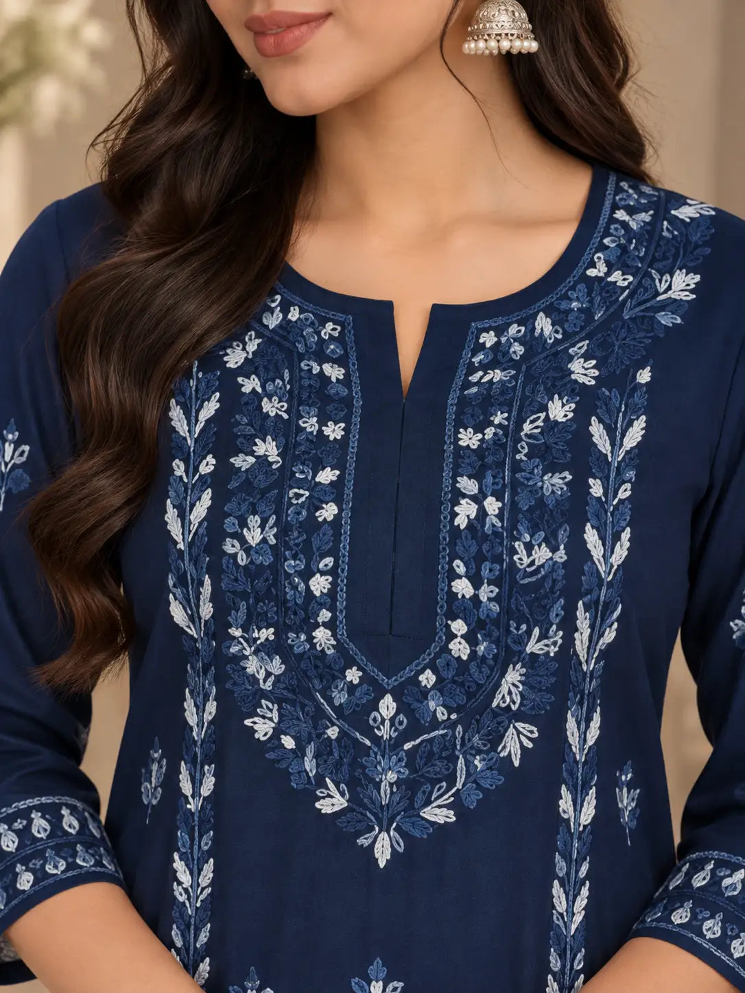 A close-up of a woman wearing a navy blue embroidered kurta with intricate white floral embroidery around the neckline and sleeves, paired with a silver jhumka earring.