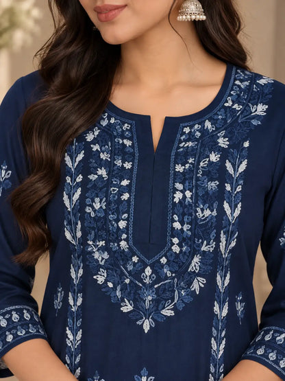 A close-up of a woman wearing a navy blue embroidered kurta with intricate white floral embroidery around the neckline and sleeves, paired with a silver jhumka earring.