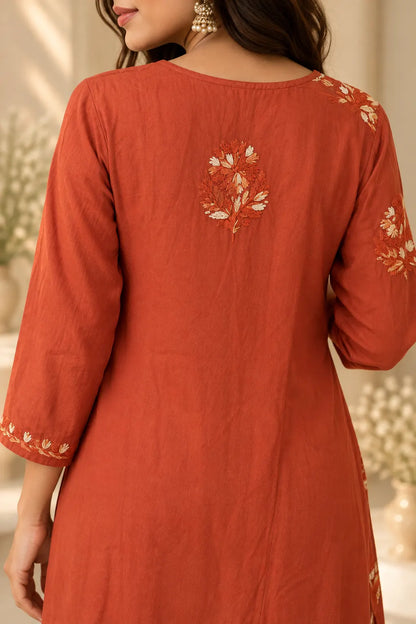 A woman wearing a rust-orange cotton kurta from the back, featuring cream and orange floral embroidery on the back neckline and sleeve cuffs.