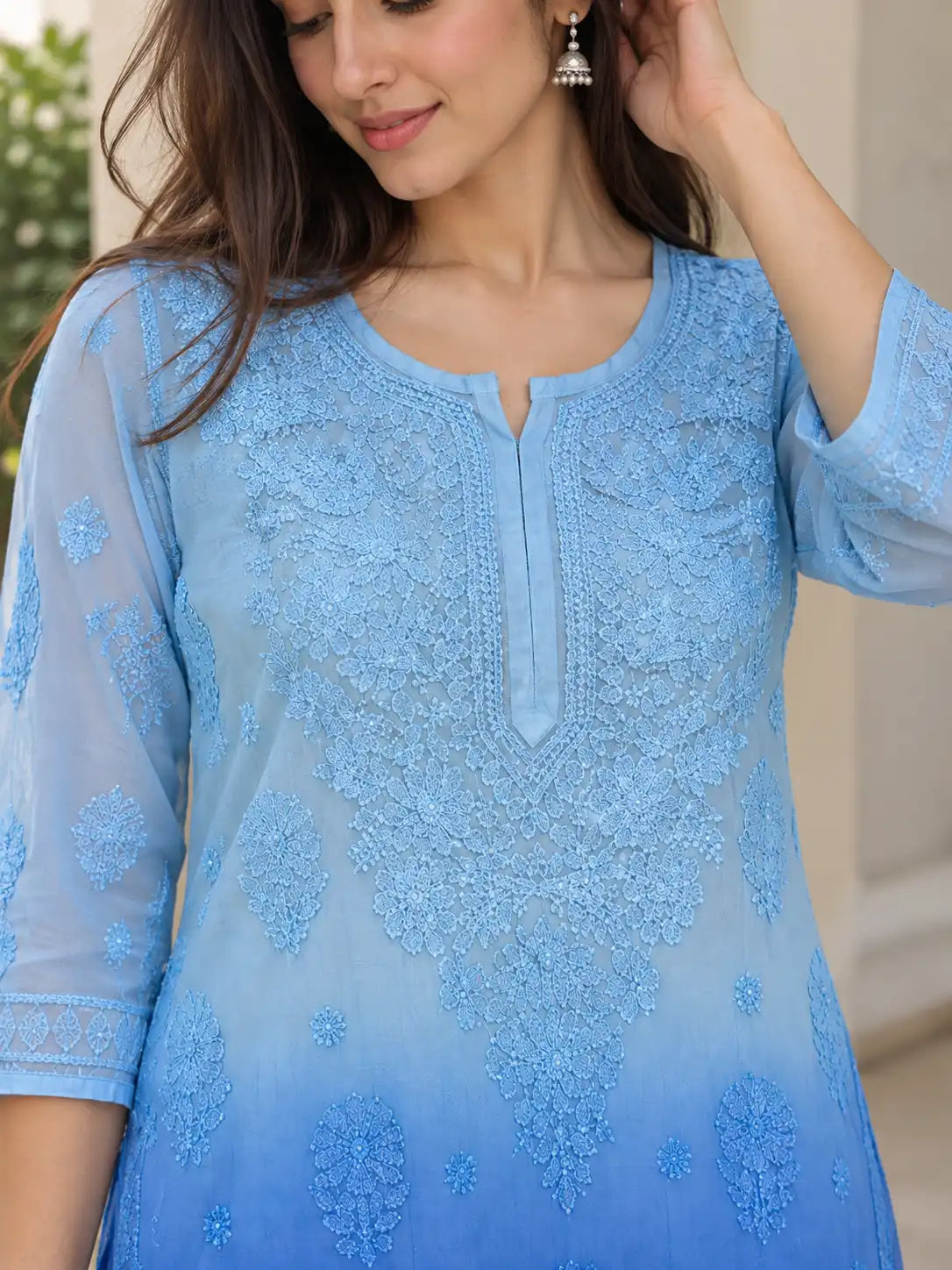A woman wearing a light blue embroidered kurta with a gradient fade to medium blue at the hem, featuring intricate floral lace embroidery and a split neckline.
