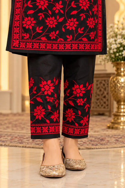 Black and red floral embroidered pants with matching red border details, shown on a model wearing gold embellished flats in an indoor setting.